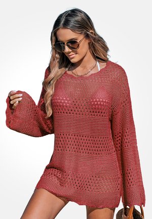 Roter gehäkelter Pullover mit lockerem Schnitt, weiten Ärmeln und Muster aus offenen Maschen. Strukturierter Stoff mit wellenförmigem Saum, getragen über einem Badeanzug.