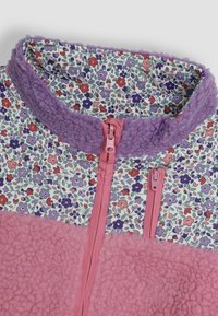 Fleece striukė su rožiniu apatiniu skyriumi, gėlėmis raštuotu viršumi, violetiniu apykakle ir dviem rožiniais užtrauktukais. Minkšta tekstūra visame gaminyje.