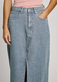 Lichtblauwe spijkerrok met een hoge taille, een split aan de voorkant en twee zijzakken; heeft een knoopsluiting en traditionele stikdetails.