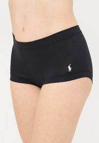 Fekete pamut elasztikus fiúshort, széles derékpánttal, bal csípőnél egy kis fehér hímezett logóval. Sima tapintás, nincs mintázat.