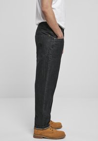 Mørk denim jeans med lige pasform, der har elastik i taljen, sidelommer og et sort broderet regnbue-logo på baglommen.
