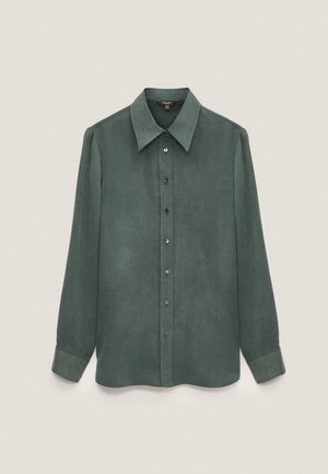Chemise boutonnée vert foncé à manches longues avec col large et poignets boutonnés sur un fond clair uni.