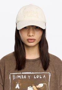 Gorra de béisbol de pana crema con el logotipo bordado "BIMBA Y LOLA" en la parte frontal, que presenta un visor curvado y una superficie texturizada.