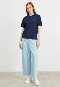 Navy blue cotton t-shirt with short sleeves and crew neck, featuring a small green logo. Paired with light blue wide-leg denim pants.