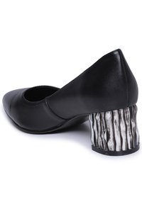 Pantofole nere in pelle con punta affusolata e tacchi curvi, caratterizzate da un design a strisce marroni e bianche testurizzate. Superficie complessivamente liscia.