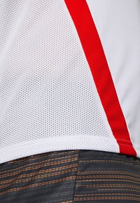 Hvidt netstof med et rødt accentpanel, der fremviser en åben vævet tekstur. Underneden mørkt materiale med orange vandrette striber.