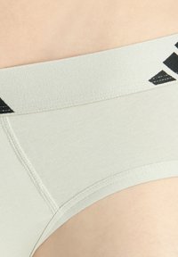 Ljusgrå kalsonger med en slät textur, med en svart logotyp på den elastiska midjebandet. Tyg som är stretchigt och kroppsnära.