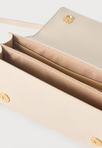 Μπεζ δερμάτινη τσάντα ώμου με χρυσά μαγνητικά κουμπιά, ανοιχτή για να εμφανίσει δύο εσωτερικά διαμερίσματα με υφασμάτινη επένδυση και ένα λεπτό λουράκι.