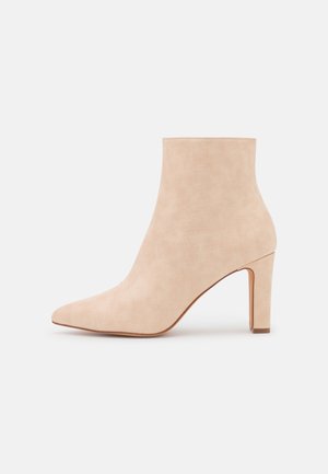 Bottine beige en daim avec bout pointu et talon bloc haut, présentée de profil sur un fond clair uni.