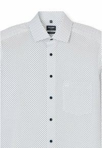 Witte blouse met zwarte stippen, modern fit ontwerp, puntige kraag en donkere knopen aan de voorkant. Heeft een borstzak.