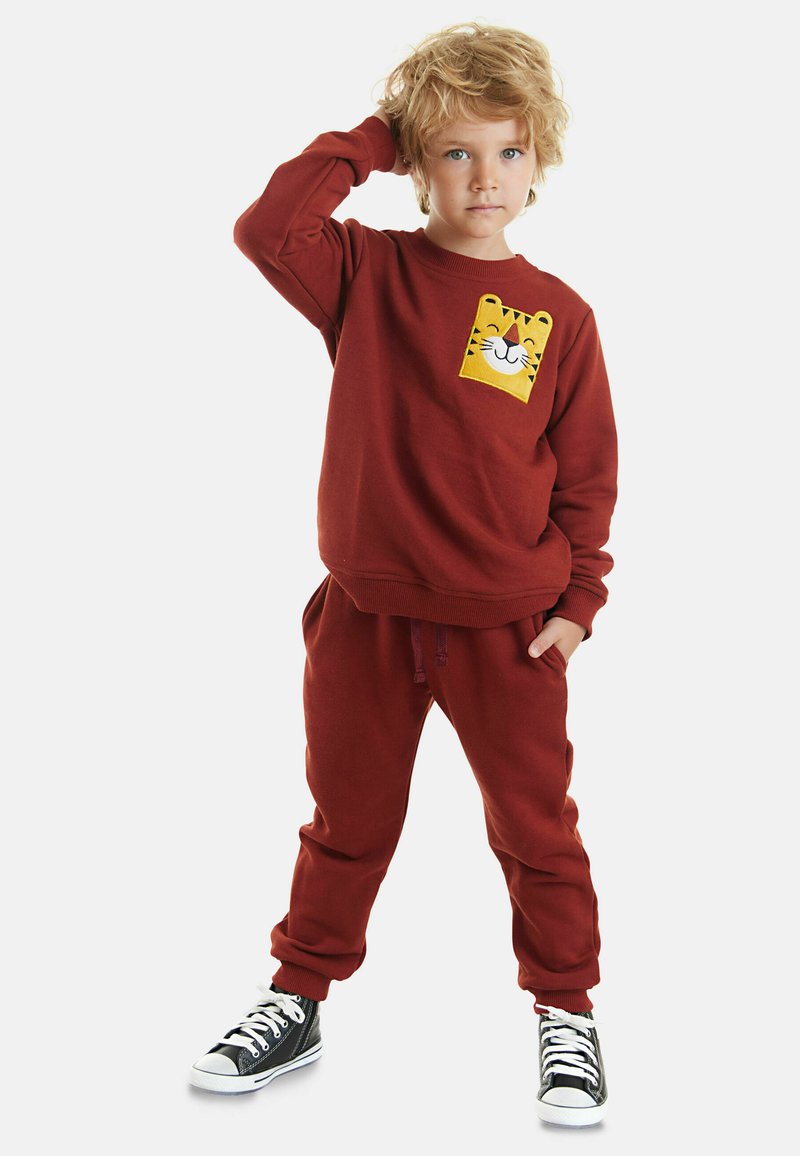 Roter Sweatshirt mit einem gelben Tigerkopf-Design auf der Tasche, kombiniert mit passenden roten Sweatpants und schwarzen High-Top-Sneakern.