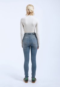 Bodysuit de manga larga en color crema combinado con jeans skinny de denim azul de talle alto. Incluye bolsillos traseros y una etiqueta en la cinturilla.
