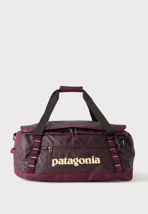 Sac de voyage Patagonia rouge foncé avec des sangles noires et une poche avant zippée sur un fond clair uni.