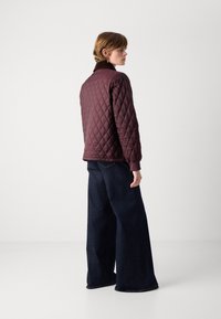 Bordeaux gewatteerde jas met ruitenpatroon, geribbelde kraag en manchetten, gecombineerd met wijde donkere denimm pantalons.