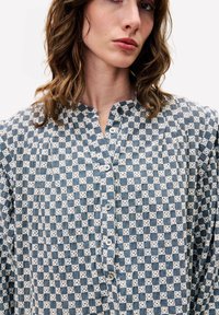 Langärmliges Hemd mit einem blau-weiß karierten Muster, ausgestattet mit einem Stehkragen und einer Knopfverschlussleiste auf der Vorderseite. Hergestellt aus einem leichten Stoff.