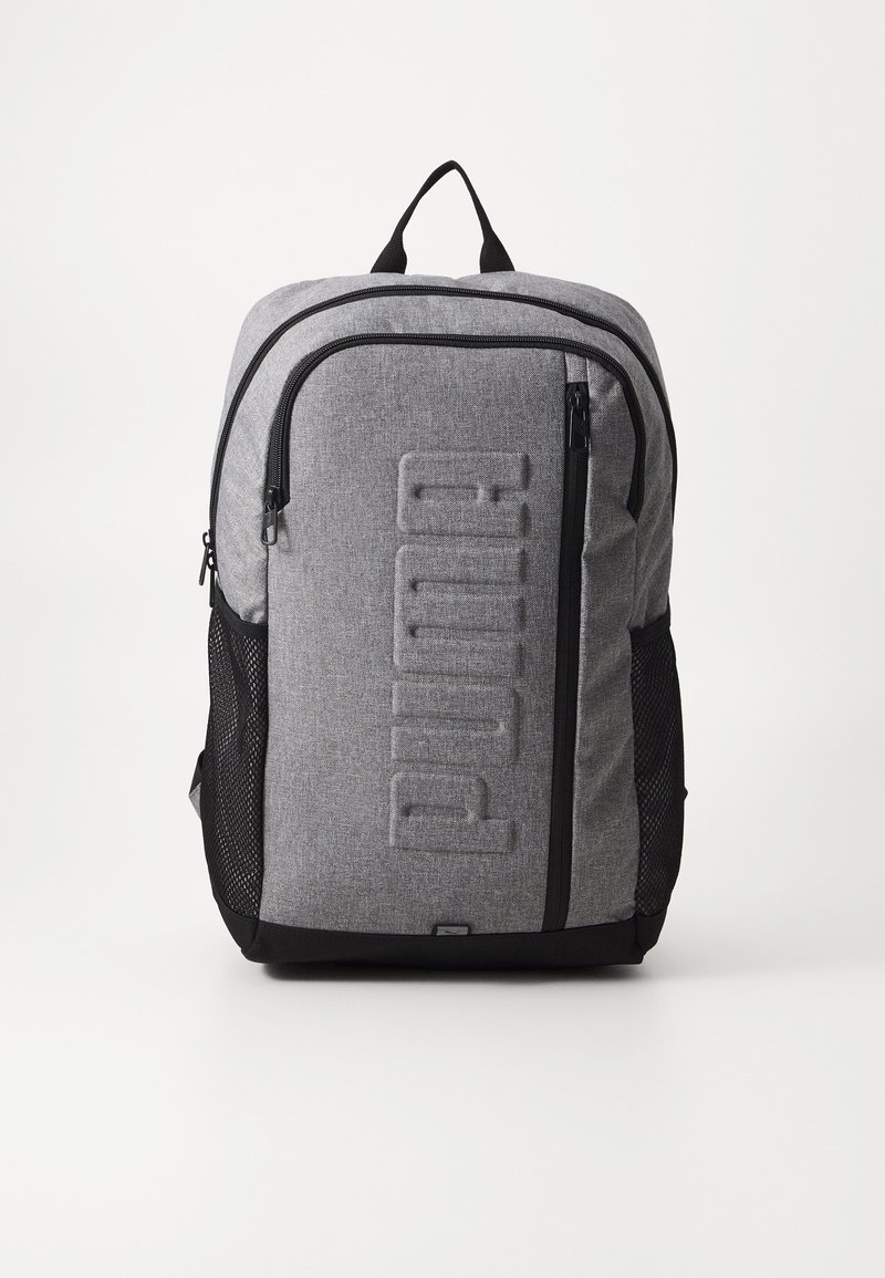 Sac à dos gris Puma avec fermetures éclair noires, poche zippée verticale à l'avant, poches latérales en mesh et poignée de transport supérieure.