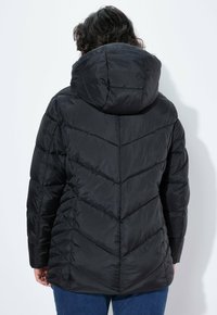 Chaqueta puffer negra con capucha, con costuras en forma de chevron y una silueta ligeramente ajustada, vista desde atrás sobre un fondo blanco.