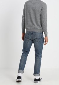 Maglione grigio a maglia, jeans blu con risvolti, sneakers nere con suola bianca e calzini bianchi. Look semplice e casual con cuciture visibili.