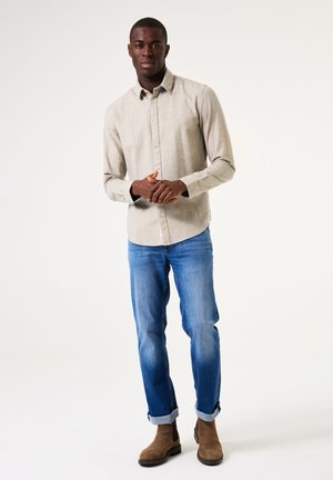Beige, button-down shirt with a textured fabric, worn with light blue jeans and brown Chelsea boots, rolled up at the cuffs.