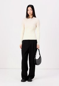 Ribbed cream long-sleeve top paired with loose black trousers and a polka-dot black handbag. Smooth texture and fitted design.