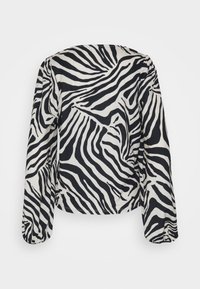 Haut à manches longues, col rond, imprimé zèbre noir et blanc, coupe ample. Tissu lisse avec un léger éclat.