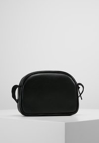 Borsa cosmetica nera in pelle, con design arrotondato, texture liscia, chiusura con zip e manico laterale per un facile trasporto.
