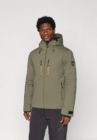 Olivovo zelená nepremokavá bunda s kapucňou, dvomi náprsnejami s oranžovými zipsami a rebrovanými detailami na pleciach. Prítomné čierne akcenty.