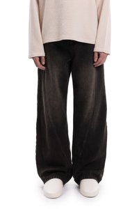 Fekete, széles szárú farmernadrág kopott hatással, íves varrásokkal és laza szabással, világos színű hosszú ujjú felsővel párosítva.