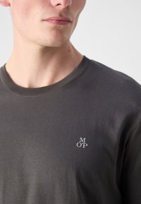 Šedé bavlnené tričko s okrúhlym výstrihom a krátkymi rukávmi, so malým bielym vyšitým logom na hrudi.