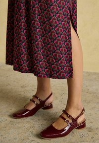 Burgunderfarbene Lackleder Slingback-Schuhe mit zwei vorderen Riemen und einem niedrigen Blockabsatz, kombiniert mit einem blumengemusterten Kleid mit seitlichem Schlitz.