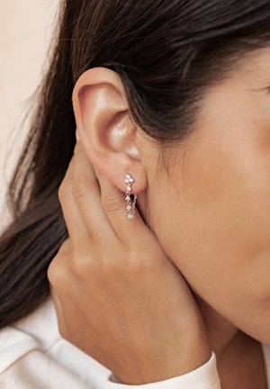 Silberne Ohrringe mit mehreren Edelstein-Akzenten, ausgestattet mit einem Haken-Design und einem zarten Kettendetail. Getragen am linken Ohr.