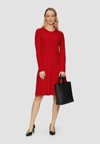 Rotes geripptes Langarmkleid mit ausgestellt Rock, kombiniert mit einer schwarzen Lederhandtasche. Glatte Textur und figurbetontes Design. Schwarze High Heels.