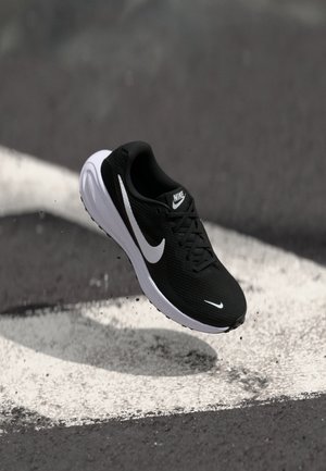 Black athletic shoe with mesh upper, white accents, and cushioned sole. Features a prominent swoosh logo and textured surface for grip.