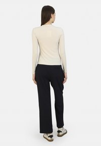 Atasan lengan panjang berwarna krem dipadukan dengan celana hitam navy yang pas. Atasan tersebut halus, sementara celananya memiliki sedikit drape. Sepatu menampilkan sol yang kontras.