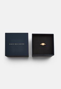 Tamno plava kutija s zlatnim logotipom "DANIEL WELLINGTON", otvorena kako bi otkrila zlatni prsten s ovalnim središnjim dijelom na crnoj jastučiću.
