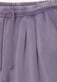 Gros plan sur un pantalon de survêtement lavande avec taille élastique, cordon de serrage et détail plissé à l'avant.