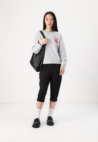 Grå sweatshirt med "01" i rød, sorte cropped bukser, sort totebag, hvite sokker og sorte chunky sko. Glatte teksturer og minimalistisk design.