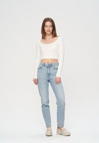 Biała prążkowana krótka bluzka z długim rękawem połączona z jasnoniebieskimi prostymi dżinsami oraz beżowymi platformami. Prosty, elegancki design bez widocznych wzorów.