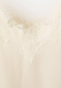 Blusa crema con un delicado borde de encaje en el escote, que presenta intrincados patrones florales y una tela suave y texturizada.