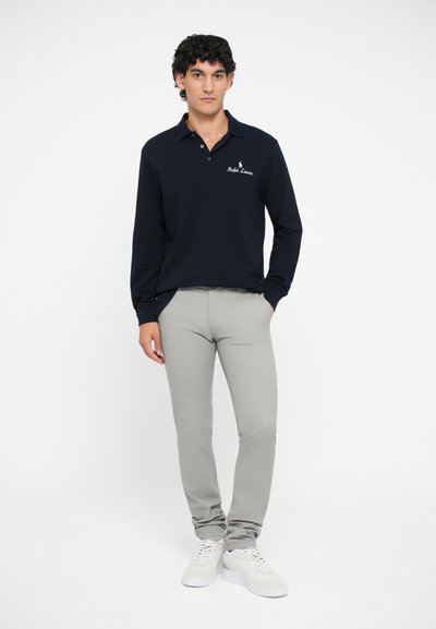 Polo de manga larga azul marino con cuello, logo en el pecho, combinado con pantalones ajustados grises claros y zapatillas blancas.