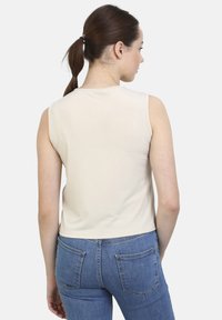 Top beige sin mangas con cuello redondo y textura suave, combinado con jeans de denim azul con bolsillos traseros y costuras visibles.