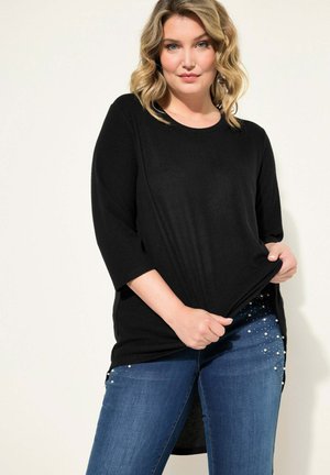 Top nero a maniche lunghe con scollatura rotonda e vestibilità morbida, abbinato a jeans blu con applicazioni di perle sulle cosce.