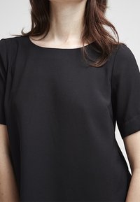 Maglietta nera a maniche corte con scollatura ampia, realizzata in tessuto liscio. Design semplice senza motivi visibili o dettagli hardware.
