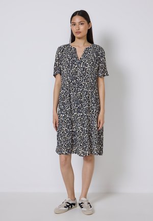 Marineblaues Kleid mit Blattmuster, kurzen Ärmeln, V-Ausschnitt und tailliertem Bund. Kombiniert mit grau-schwarzen Sneakers. Glattes, leichtes Material.
