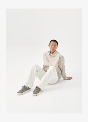 Beige skjorte med knapper, hvite bukser og grå sneakers. Skjorten har en løs passform, og sneakersene har en teksturert overflate og snøring.