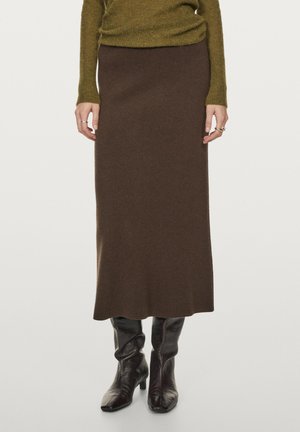 Jupe en tricot marron avec une silhouette droite, coupée jusqu'au mi-mollet. L'association avec des bottes noires à bout effilé accentue le design.