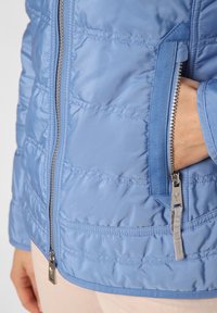 Hellblau isolierte Jacke mit einem Reißverschluss vorne, horizontalen Nähten und seitlichen Taschen mit eleganten Hardware-Akzenten.