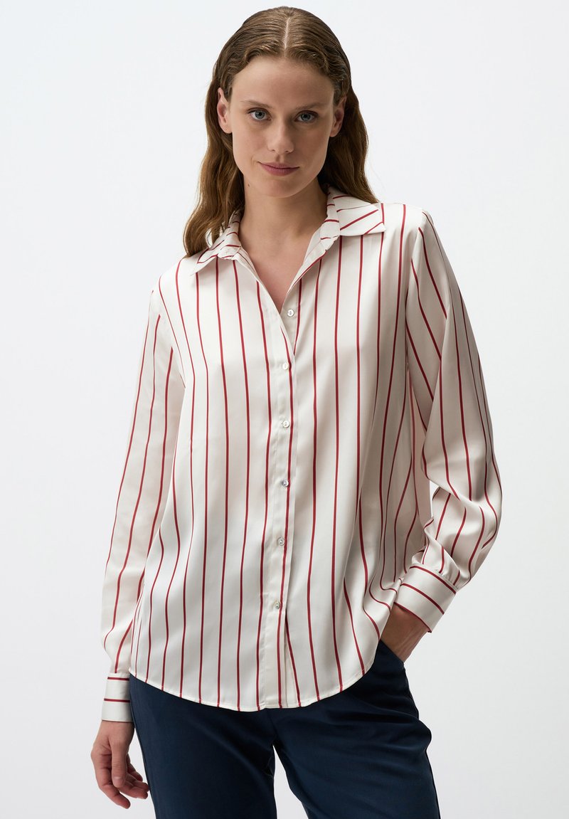 Camicia bianca con righe verticali rosse, maniche lunghe e colletto a punta. Tessuto liscia con una leggera lucentezza, orlo curvo.