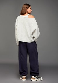 Ljusgrå off-shoulder tröja kombinerad med marinblå baggy sweatpants och silverfärgade sneakers. Mjuk textur och avslappnad passform för komfort.