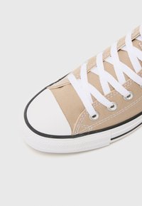 Beiger Leinensneaker mit einer weißen Gummikappe, schwarzem Besatz und weißen Schnürsenkeln. Verfügt über metallische Ösen und eine strukturierte Gummisohle.
